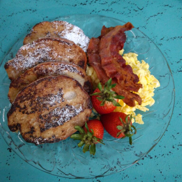 Breakfast of French Toast with scrambled eggs and bacon with garnish of strawberries
